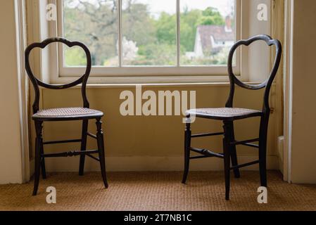 Zwei alte hölzerne Stühle sitzen vor einem großen Schiebefenster in einem großen Anwesen in Suffolk England in Großbritannien Stockfoto