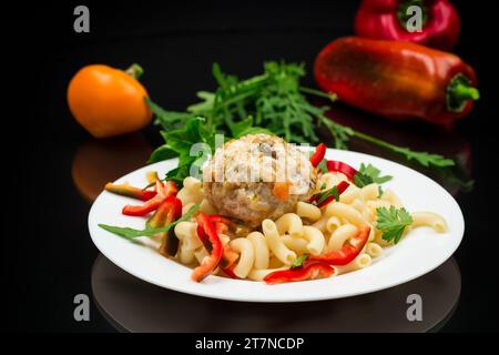Gekochte Pasta mit Fleischbällchen, Paprika und Kräutern mit Gewürzen auf einem Teller, isoliert auf schwarzem Hintergrund Stockfoto