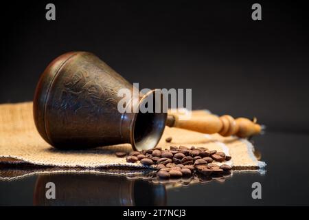 Natürliche Kaffeebohnen, türkische Kaffeekanne auf Sackleinen, isoliert auf schwarzem Hintergrund Stockfoto