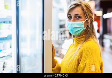 Nahaufnahme einer Frau in einem gelben Pullover mit Maske beim Einkaufen Stockfoto