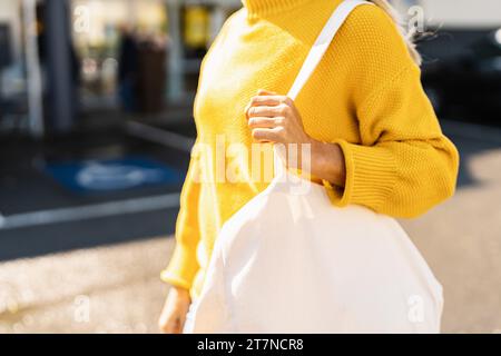 Nahaufnahme einer Frau in einem gelben Pullover mit einer weißen Tragetasche Stockfoto