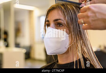 Frau, die während der covid-19-Pandemie den Friseur besucht und ein neues Styling mit FFP2-Gesichtsmaske erhält Stockfoto
