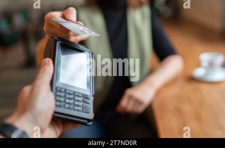 Junge Frau mit Kredit, die drahtlose Bankzahlung mit POS-Terminal-Prozess macht, erwerben am Tisch im Café-Restaurant im Innenbereich. Konzentriere dich auf die Maschine Stockfoto