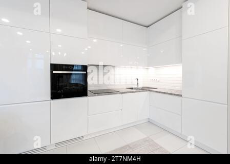 Moderne Inneneinrichtung. Küche mit Waschbecken und schwarzem Ofen. Weiße Möbel. LED-Leuchte. Luxuriöses Zuhause. Stockfoto