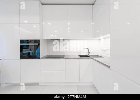 Moderne Inneneinrichtung. Küche mit Waschbecken und schwarzem Ofen. Weiße Möbel. LED-Leuchte. Luxuriöses Zuhause. Stockfoto