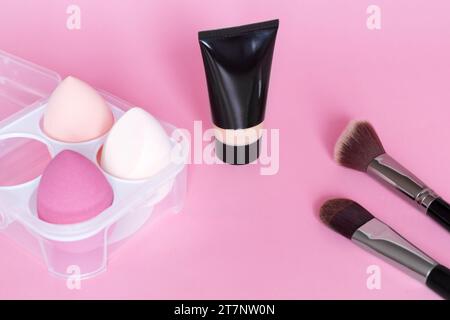 Make-up Foundation, Make-up Schwamm und Pinsel auf rosa Hintergrund. Kosmetisches Werkzeugkonzept. Kosmetikaccessoires. Stockfoto