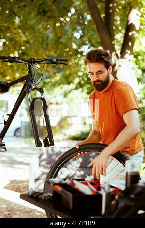 Im Hof zu Hause benutzt ein junger, energischer Mann professionelle Werkzeuge, um beschädigtes Rad zu ersetzen. Der Service auf zerlegtem Fahrrad im Freien für das Vergnügen Radfahren ist ein engagierter, gesunder kaukasier männlicher Radfahrer. Stockfoto