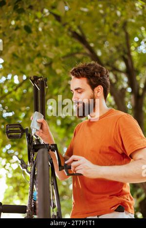 Fokussierter und aktiver Mensch, der moderne Fahrradketten für die jährliche Wartung im Sommer schmiert und wartet. Detaillierte Abbildung, die männliche kaukasier zeigt, wie sie im Außenbereich die Pedale des Fahrrads gekonnt schmiert. Stockfoto