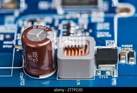 Nahaufnahme von Induktivität, Elektrolytkondensator oder Transistor auf unscharfem Leiterplattenhintergrund. Blaue Stromversorgungsplatine mit elektronischen Komponenten. Stockfoto