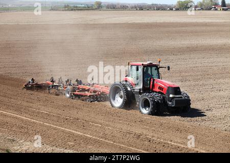 Ein Traktor auf einem Bauernhof, der ein Pfluggerät zieht, pflügt und belüftet den Boden zur Vorbereitung auf das Anpflanzen von Idaho-Kartoffeln im Frühjahr. Stockfoto