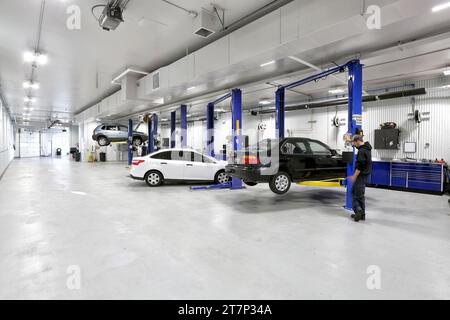 Ein Mechaniker, der ein Auto auf einem hydraulischen Aufzug hochfährt, in einer neuen, modernen Autowerkstatt. Stockfoto