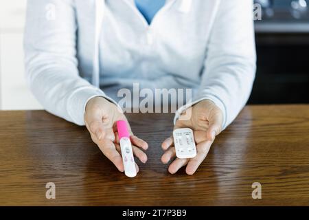 Frau mit positivem Schwangerschaftstest und positivem COVID-Test. Schwangere Frauen, die krank sind, können keine Medikamente einnehmen. Stockfoto