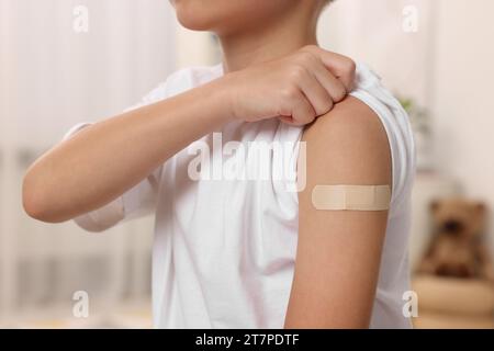 Junge mit klebendem Pflaster am Arm nach der Impfung drinnen, Nahaufnahme Stockfoto