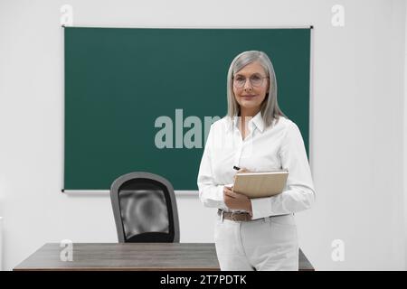 Porträt des Professors mit Notizbuch in der Nähe der Tafel im Klassenzimmer, Raum für Text Stockfoto