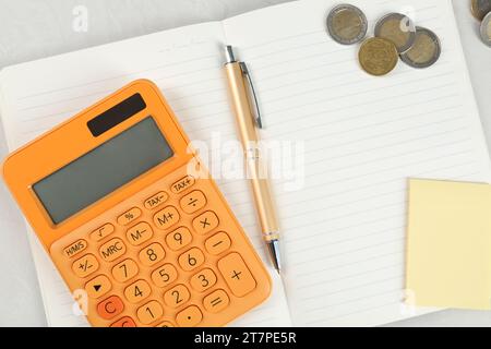 Taschenrechner, Notizbuch, Stift, Münzen und Haftnotiz auf hellgrauem Tisch, flach gelegt. Altersvorsorgekonzept Stockfoto