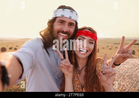 Glückliches Hippie-Paar, das Friedenszeichen zeigt, während es Selfie im Feld macht Stockfoto