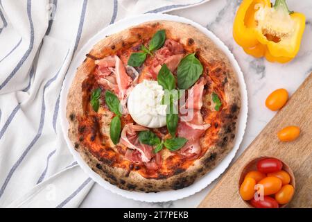 Köstliche Pizza mit Burrata, Basilikum, Schinken und Gemüse auf weißem Marmortisch, flach gelegen Stockfoto