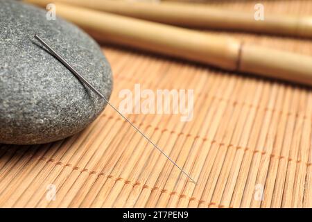 Akupunkturnadel und Spa-Stein auf Bambusmatte, Nahaufnahme. Leerzeichen für Text Stockfoto