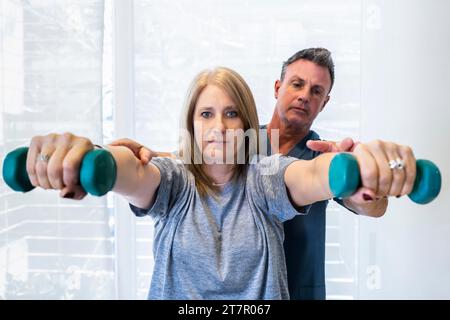 Männlicher Physiotherapeut, der einem Patienten beibringt, wie man Kurzhanteln zur Wohlbefinden- und Behindertenunterstützung verwendet Stockfoto