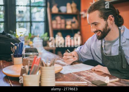 happy pottery artist designer enjoy sketch design handmade clay mug cup work small business workshop Stockfoto