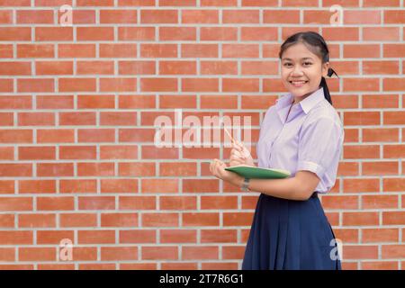 Porträt thailändischer asiatischer Schüler in Uniform stehend Lächeln mit Bleistift und Taschennotizbuch Stockfoto
