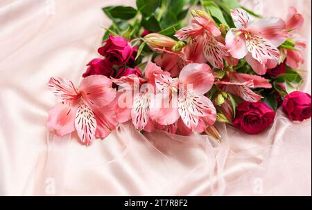 Schöne rosa Alstroemeria und Rosen Blumen auf weichem rosa Seidenhintergrund. Stockfoto