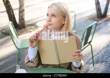 Porträt einer jungen kreativen Frau, die im Freien skizziert, mit Notizbuch und Stift im Café sitzt, Kunst zeichnet und lächelt Stockfoto