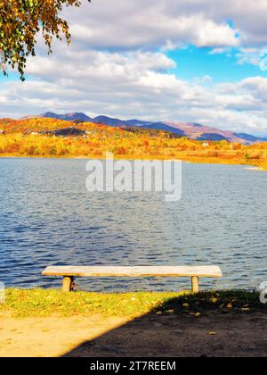 Holzbank am Ufer eines Sees. Farbenfrohe Landschaft an einem sonnigen Herbsttag. Reise- und Entspannungskonzept Stockfoto