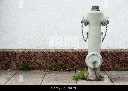 Ein weißer Hydrant befindet sich an der Seite eines Betongehäuses in einem städtischen Bereich Stockfoto