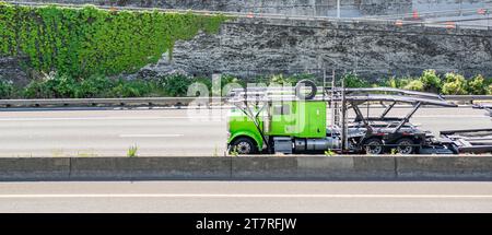 Industrieller grüner Pkw-Transportträger großer Lkw-Sattelzugmaschine für den Transport leerer hydraulischer Auflieger Fahren auf der geteilten Autobahn mit konc Stockfoto