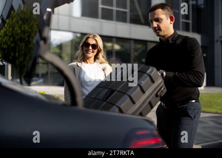 Geschäftsfrau wartet, während der Chauffeur einen Koffer in den Kofferraum packt und während einer Geschäftsreise ein luxuriöses Taxi nutzt. Konzept des Business Transfer Service Stockfoto