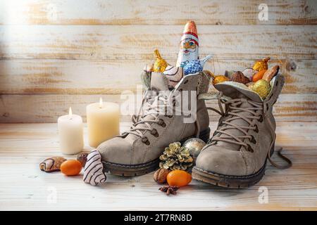 Winterstiefel, Süßigkeiten, Weihnachtsdekoration und ein Schokoladensmann gegen rustikales Holz, Tradition am Nikolaustag oder im deutschen Nikolaus Tag zum Füllen des Schuhs Stockfoto