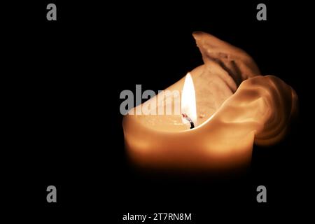 Weiße Kerze mit Flamme und schmelzendem Wachs am Rand vor schwarzem Hintergrund, Licht im Dunkeln zu Weihnachten, Advent oder Neujahr, Kopierraum, Sell Stockfoto