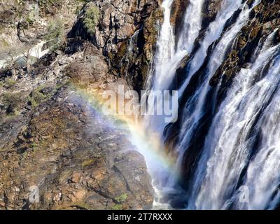 Eine atemberaubende Landschaft mit einem majestätischen Wasserfall, der einen felsigen Berg hinabstürzt, mit einem lebhaften Regenbogenbogen, der sich am fernen Himmel darüber erhebt Stockfoto