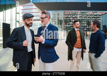 Eine Gruppe von Geschäftsleuten, die die Investition auf einem Handy beobachten. Geschäftsleute, die ein Smartphone verwenden, um im Internet zu surfen. Ein Angestellter, der seinem Startup-Partner seinen Handy-Bildschirm zeigt. Hochwertige Fotos Stockfoto