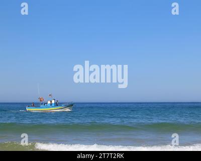 Almada, Portugal. 22. August 2023: Kleines traditionelles Fischerboot segelt über den Strand Fonte da Telha an der Costa da Caparica Küste mit Atlantik Stockfoto