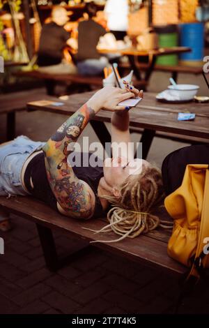 Eine junge Frau liegt auf einer Bank und schreibt eine Nachricht auf einem Smartphone. Stockfoto