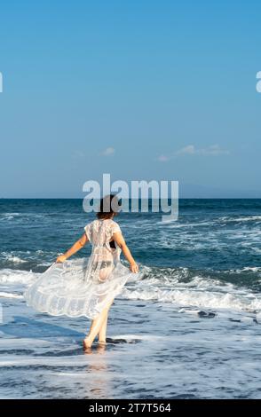 Junge attraktive Frau in schwarzem Bikini, die an einem schwarzen Sand vorbeiläuft Stockfoto