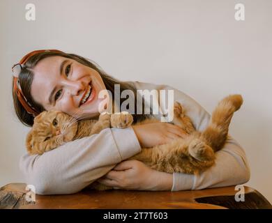 Glückliche junge Frau mit einer orangen Scottish Fold Katze, beide lächeln Stockfoto