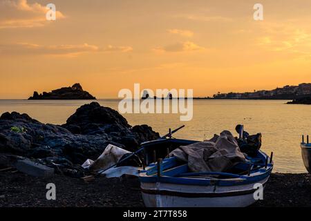 Altes Fischerboot, das am Kieselstrand in der Nähe von Isola Lachea, der berühmten Zyklopeninsel in Homers Odyssee, bei Sonnenuntergang in Sizilien, Italien, gestrandet ist Stockfoto