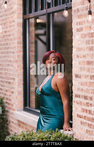 Schwarzes Mädchen mit roten Haaren und grünem Kleid auf Ziegelfensterbank Stockfoto