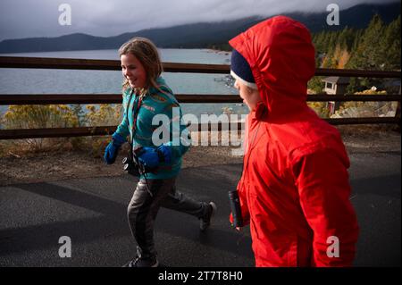 Zwei Zwillingsgeschwister, die im Herbst am Lake Tahoe entlang laufen Stockfoto