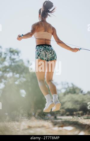 Eine weiße Frau springt mit Freunden im Park ins Seil. Sie genießt einen sonnigen Tag und übt fit Körper, positive Motivation und gesunden Lebensstil. Stockfoto