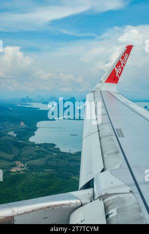 Flügel eines Air Asia Flugzeugs, das an einem sonnigen, aber trüben Tag über die Inseln der Andamanensee nach Phuket fliegt Stockfoto