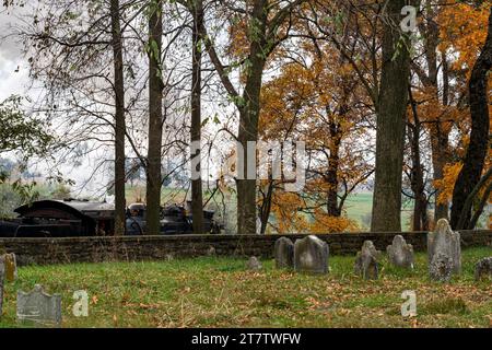 Blick auf eine Dampflok, die an einem alten Friedhof vorbeifährt und an einem Herbsttag Rauch bläst Stockfoto