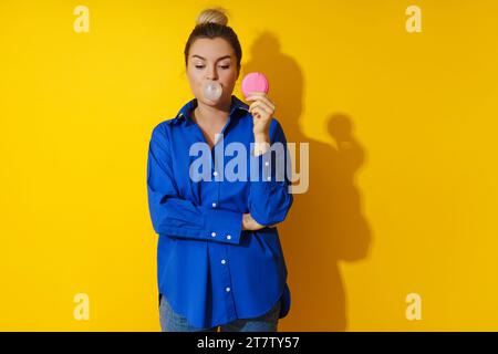 Glückliche Frau, die eine Blase mit Kaugummi vor gelbem Hintergrund bläst Stockfoto