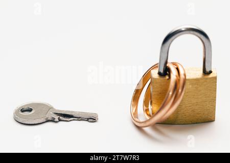 Kleiner Schlüssel und zwei goldene Eheringe, die auf einem Vorhängeschloss verschlossen sind Stockfoto