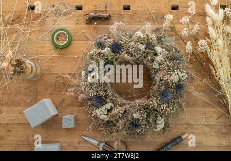 Blick von oben auf einen Blumenkranz auf einem Holztisch zwischen Blumenwerkzeugen und Bastelmaterialien Stockfoto