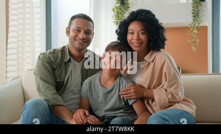 Multirassisches afroamerikanisches Kaukasisches glückliches Familienporträt zu Hause lächelnde Eltern Vater und Mutter umarmen kleinen Jungen Kind im Vorschulalter auf Sofa Stockfoto