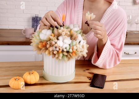 Strauß aus getrockneten Blumen als Geschenk für den Urlaub. Frau im Hausmantel mit einem Strauß getrockneter Blumen in der Küche. Stockfoto